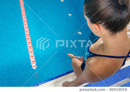 Young woman touching water with foot in indoor swimming pool Young woman touching water with foot in indoor swimming pool 80410059