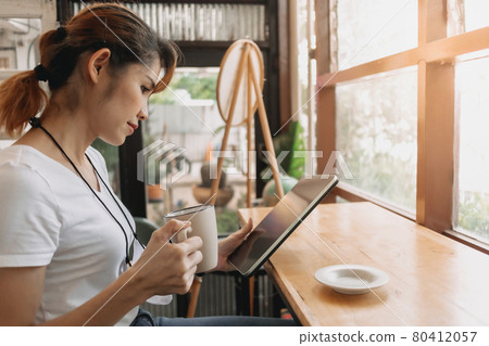 Woman is looking at the tablet and drinking coffee in the cafe. 80412057