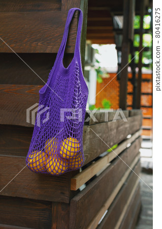 yellow lemons in purple string bag hang on wooden veranda 80416275