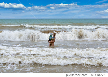 A woman carries in her arms a child from a stormy sea A woman carries in her arms a child from a stormy sea 80418776
