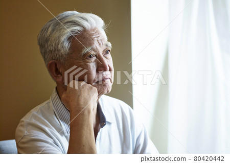 portrait of a sad asian senior man sitting by the window hand on chin 80420442
