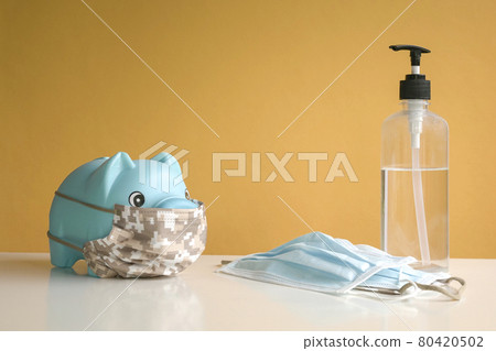 Piggy bank wearing protective face mask and hand sanitizer on yellow background. 80420502