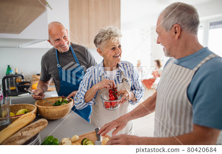 Group of senior friends having party indoors, cooking and talking. Group of senior friends having party indoors, cooking and talking. 80420684