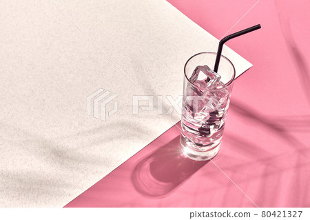 Glass of mineral water with ice on pink and white background with shadow from a palm leaf Glass of mineral water with ice on pink and white background with shadow from a palm leaf 80421327
