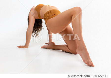 Portrait of young beautiful tanned slim caucasian woman in mustard underwear posing on floor over white background. 80422512
