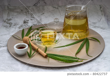 Refreshing and enjoy with A cup of Cannabis herbal tea and Stem with green marijuana leaves with honey on marble table. Refreshing and enjoy with A cup of Cannabis herbal tea and Stem with green marijuana leaves with honey on marble table. 80422737
