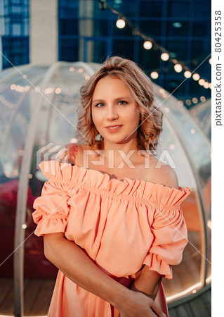portrait of an attractive woman in a pink dress in a rooftop cafe 80425358