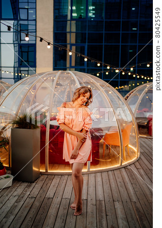 an attractive woman in a pink dress in a rooftop cafe 80425549
