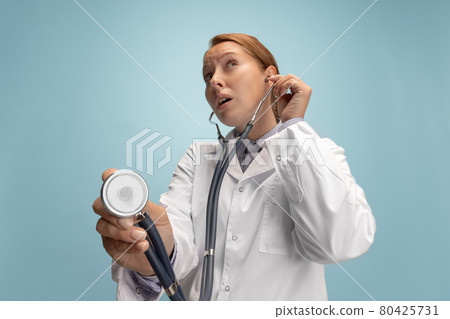 Close-up female doctor, therapeutic or medical advisor with stethoscope at work isolated over blue studio background. Concept of healthcare, care medicine and humor Close-up female doctor, therapeutic or medical advisor with stethoscope at work isolated over blue studio background. Concept of healthcare, care medicine and humor 80425731