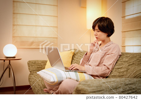 Young woman looking at a computer on the sofa Young woman looking at a computer on the sofa 80427642