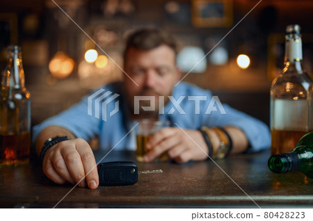 Drunk man with car key sitting at counter in bar 80428223