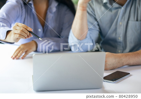 Two young people, colleguas during working day, business meeting. Using laptop, modern gadgets, notes. Workplace at office with PC, devices. Two young people, colleguas during working day, business meeting. Using laptop, modern gadgets, notes. Workplace at office with PC, devices. 80428950