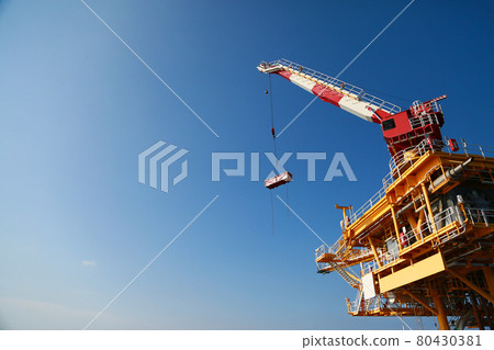 Oil and gas platform standing in the gulf or offshore and operation by technician. Crane moving any cargo or tools basket from supply boat to the platform. Heavy lift was moving by crane technician. 80430381
