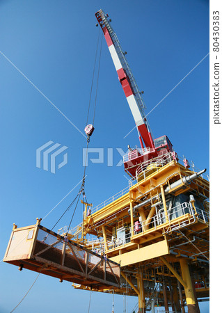 Oil and gas platform standing in the gulf or offshore and operation by technician. Crane moving any cargo or tools basket from supply boat to the platform. Heavy lift was moving by crane technician. 80430383