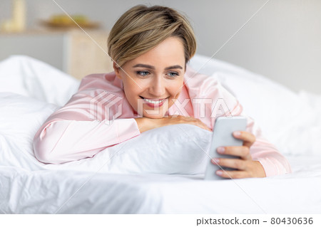 Happy woman lying in bed reading text message Happy woman lying in bed reading text message 80430636