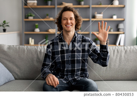 Positive Man Waving Hello In Greeting Gesture Sitting At Home Positive Man Waving Hello In Greeting Gesture Sitting At Home 80430853