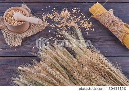 Top view wheat grains with mortar grinder and spaghetti on dark wood. 80431138