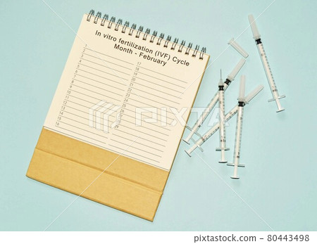 February IVF cycle calendar and disposable injection syringe on blue background 80443498
