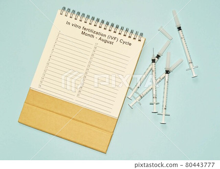 August IVF cycle calendar and disposable injection syringe on blue background 80443777