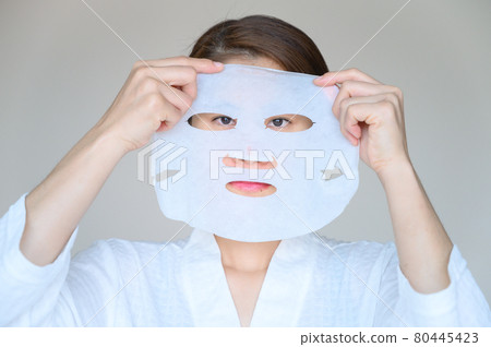 Portrait of young woman holding facial mask befor applying to enhance her skin and looking to camera. Facial mask is a creamy or thick pasted mask applied to clean or smoothen the face. 80445423