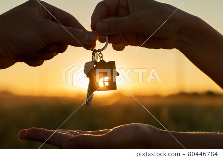 Close-up female gives a man the key to a new house on the background of a beautiful sunset. The concept of construction and real estate transactions. 80446784