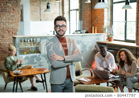 Young smiling businessman standing in front of working colleagues Young smiling businessman standing in front of working colleagues 80447797