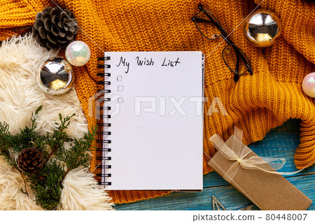 Flat lay New Year decorations and blank white spiral notebook with My wishlist framed with yellow cozy winter decor, tree branches, xmas toys. Planning,wish list 2022 concept. 80448007