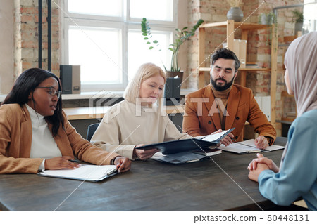 Mature blond female looking through resume of young Muslim woman 80448131