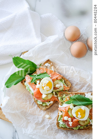 Open sandwich traditional danish smorrebrod salmon, cucumber, boiled egg, soft cheese. Homemade sandwich with rye bread on white background, top view. Tasty salmon fish sandwich closeup Open sandwich traditional danish smorrebrod salmon, cucumber, boiled egg, soft cheese. Homemade sandwich with rye bread on white background, top view. Tasty salmon fish sandwich closeup 80448284