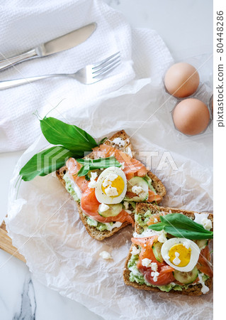 Open sandwich traditional danish smorrebrod salmon, cucumber, boiled egg, soft cheese. Homemade sandwich with rye bread on white background, top view. Tasty salmon fish sandwich closeup 80448286