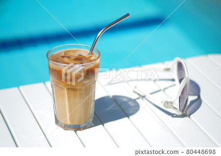 Ice coffee Cyprus Frappe Fredo against blue clear water of the swimming pool, on white table, with sunglasses. Summer minimalistic background, holiday or vacation concept. Sun and shadows.Copy space 80448698