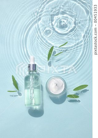 Set moisturizing cosmetic products on water with drops. Glass bottle with serum, jar of cream 80451933