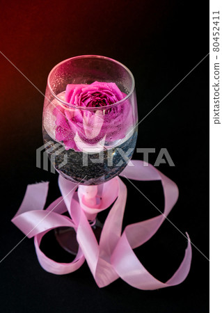 Wine glass filled with pink flower petalson table with black. Minimal modern still life. Holiday concept Valentines or womans day background design Wine glass filled with pink flower petalson table with black. Minimal modern still life. Holiday concept Valentines or womans day background design 80452411