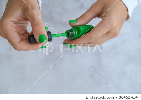 Manicured female hands with stylish green nails holding bottle of nail polish. Trendy modern design manicure. Gel nails. Skin care. Beauty treatment. Nail care. Trendy colors Manicured female hands with stylish green nails holding bottle of nail polish. Trendy modern design manicure. Gel nails. Skin care. Beauty treatment. Nail care. Trendy colors 80452414