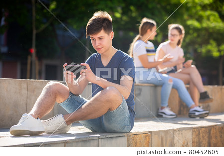 Teen boy with phone on summer city street 80452605