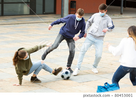 Teenagers in masks playing soccer outside 80453001