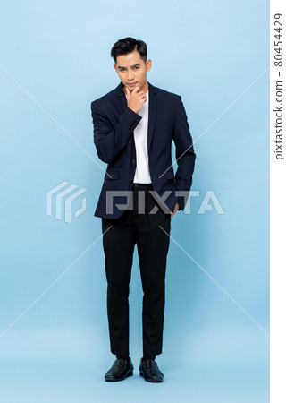 Young handsome Asian businessman standing and posing with hand touching chin Young handsome Asian businessman standing and posing with hand touching chin 80454429