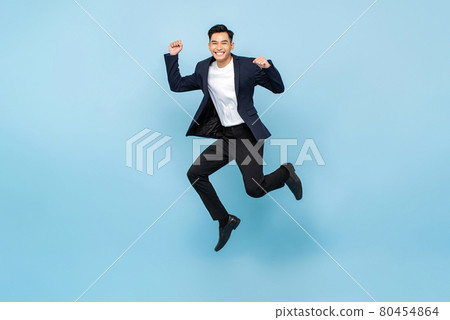 Ecstatic handsome Asian man jumping and raising  his fists on isolated light blue studio background 80454864