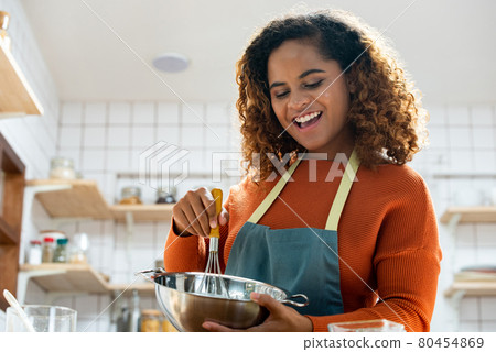 Young pretty African American woman enjoying herself cooking in kitchen while staying at home 80454869