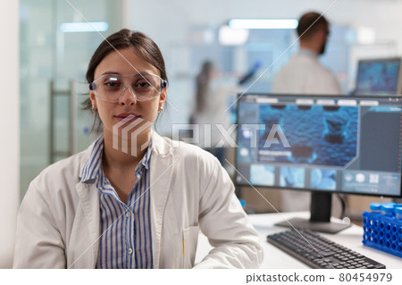 Scientist with lab coat sitting in laboratory looking at camera smiling Scientist with lab coat sitting in laboratory looking at camera smiling 80454979