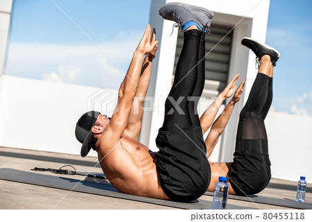 Group of athletic men doing toe touch crunch workout exercise outdoors on building rooftop floor Group of athletic men doing toe touch crunch workout exercise outdoors on building rooftop floor 80455118
