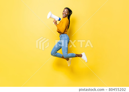 Joyful young African American woman holding megaphone jumping and making announcement Joyful young African American woman holding megaphone jumping and making announcement 80455202