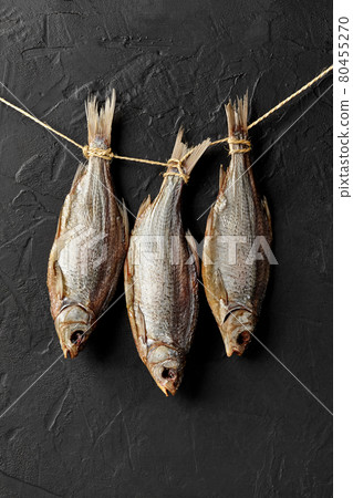 Dried salted roach fish hanging on rope on black wall 80455270
