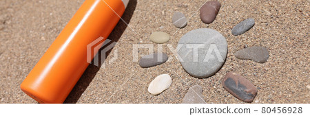 Sunscreen lotion lies on hot sand next to sun figure made of stones Sunscreen lotion lies on hot sand next to sun figure made of stones 80456928