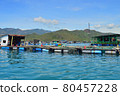 a floating fishing village in a sea bay, against a backdrop of mountains covered with tropical vegetation, clouds and a blue sky 80457228