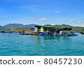 a floating fishing village in a sea bay, against a backdrop of mountains covered with tropical vegetation, clouds and a blue sky 80457230