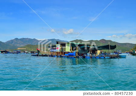 a floating fishing village in a sea bay, against a backdrop of mountains covered with tropical vegetation, clouds and a blue sky 80457230