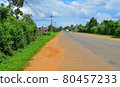 a provincial road, with buses traveling along it, people riding mopeds, against the backdrop of a bright green prastity, a blue sky covered with clouds 80457233