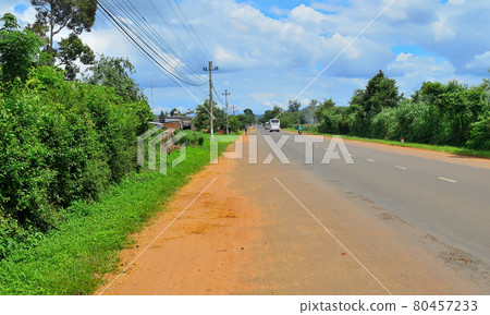 a provincial road, with buses traveling along it, people riding mopeds, against the backdrop of a bright green prastity, a blue sky covered with clouds a provincial road, with buses traveling along it, people riding mopeds, against the backdrop of a bright green prastity, a blue sky covered with clouds 80457233