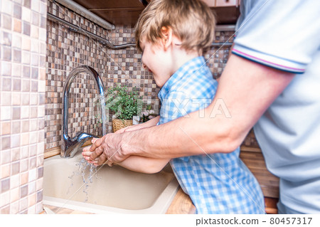 Cheerful son and his father washing hands together with soap and water in bathroom. Man and little Boy Stay safety at home and hygiene concept. Selective focus and blur people. Cheerful son and his father washing hands together with soap and water in bathroom. Man and little Boy Stay safety at home and hygiene concept. Selective focus and blur people. 80457317